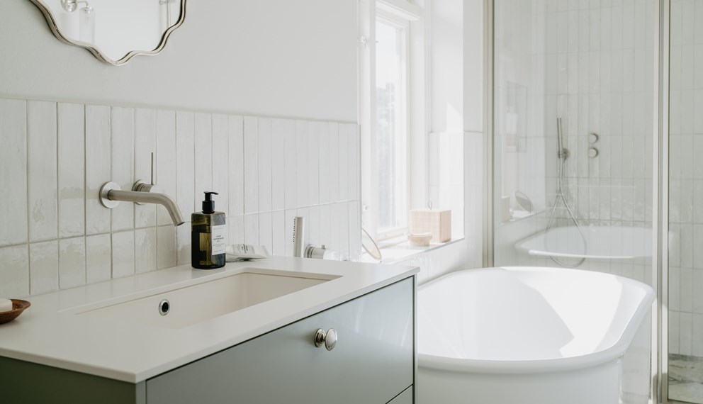 Lyst, landlig baderom med badekar, hvite fliser og lysegrønn baderomsinnredning