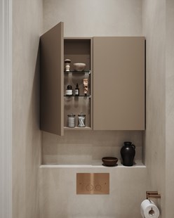 Grunt veggskap i fargen Warm Clay over toalettet, med åpne dører som viser baderomsartikler og detaljer i bronse.