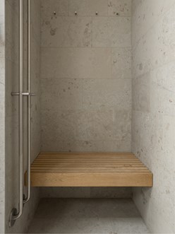 Dusjnisje med vegger i kalkstein og sittebenk i tre, kombinert med detaljer i børstet stål.  