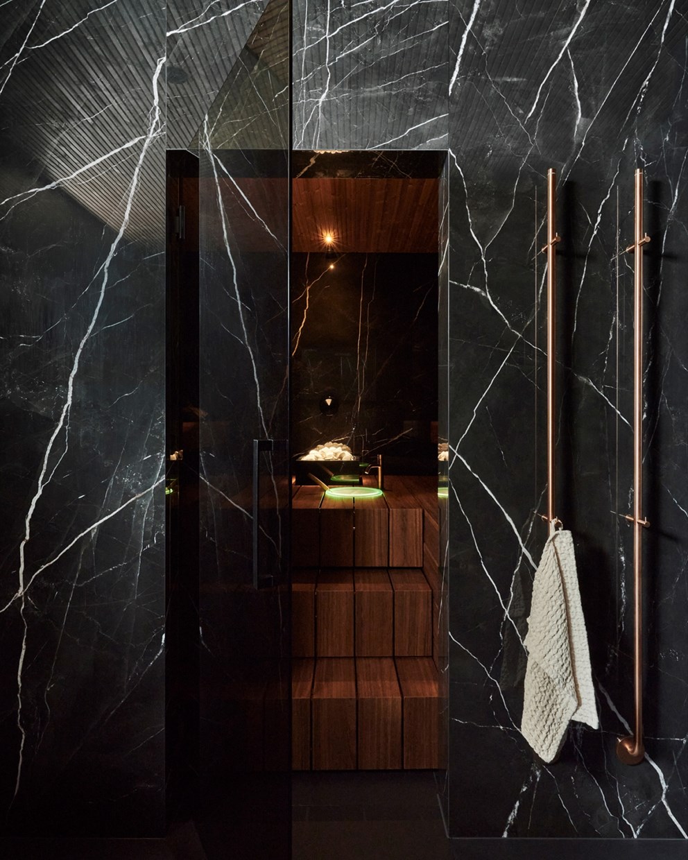 Badstue med innrammende vegger i svart marmor, treinteriør og bronsefargede detaljer.