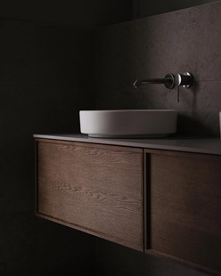 Baderomsinnredning i mørk eik med rund hvit bolleservant og vegghengt armatur i børstet metall.